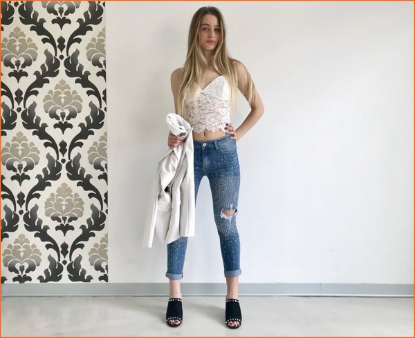 Jeans rotture e borchiette con crop top pizzo bianco e giacca ecopelle.